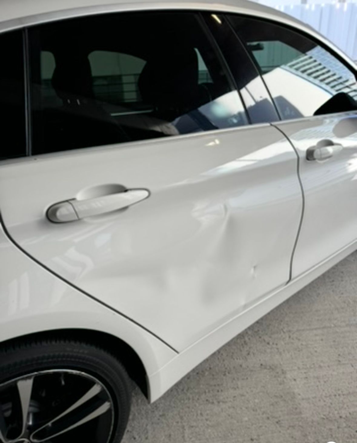A white BMW with a deep dent in the rear door